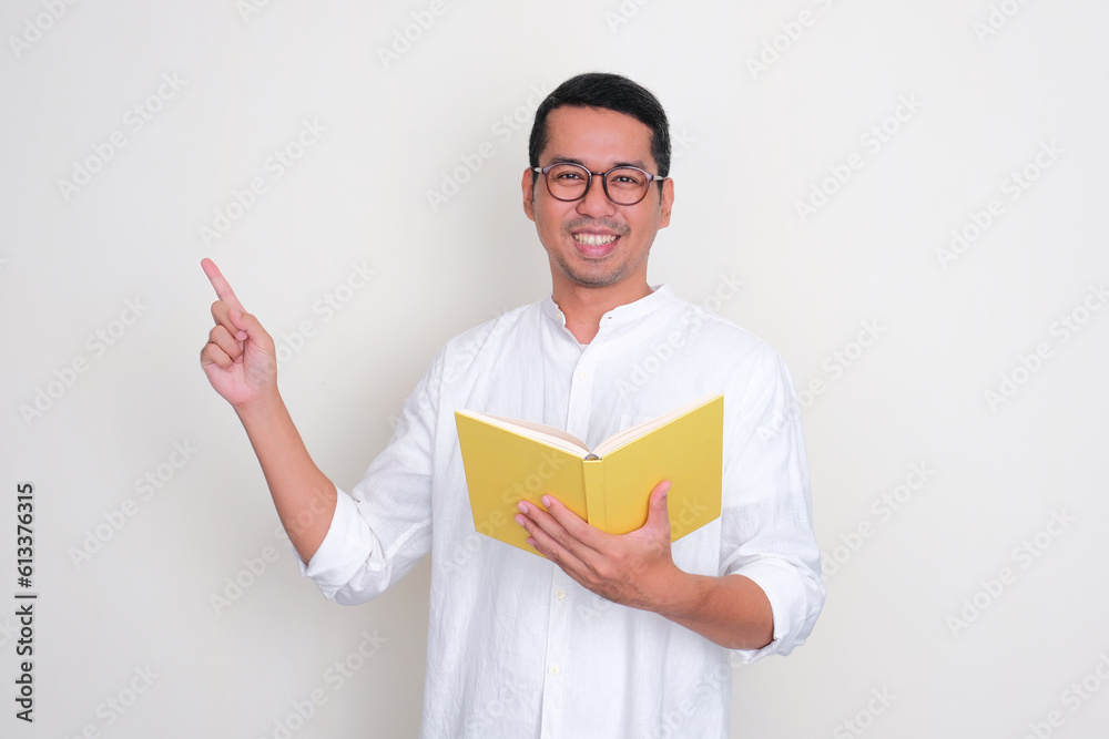 Adult Asian man smiling and pointing to the right side while holding a book Adult Asian man smiling and pointing to the right side while holding a book