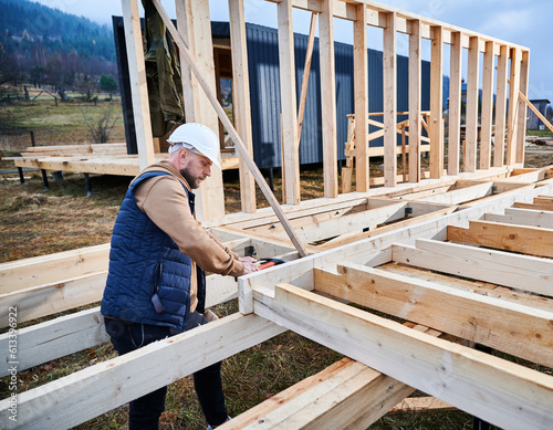 Man worker building wooden frame house on pile foundation. Carpenter hammering nail into wooden truss, using hammer. Carpentry concept.