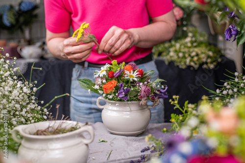 Florist bei der Arbeit, Frau steckt ein Blumengesteck aus frischen bunten Blumen in Gefäße aus Keramik