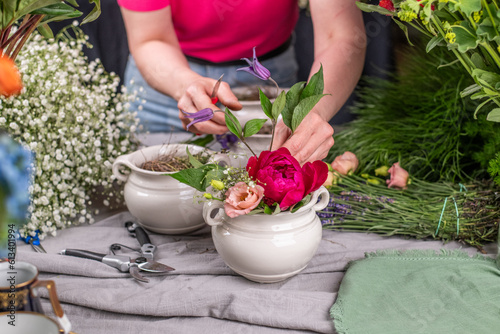 Florist bei der Arbeit, Frau steckt ein Blumengesteck aus frischen bunten Blumen in Gefäße aus Keramik