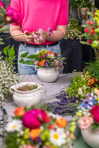 Florist bei der Arbeit, Frau steckt ein Blumengesteck aus frischen bunten Blumen in Gefäße aus Keramik