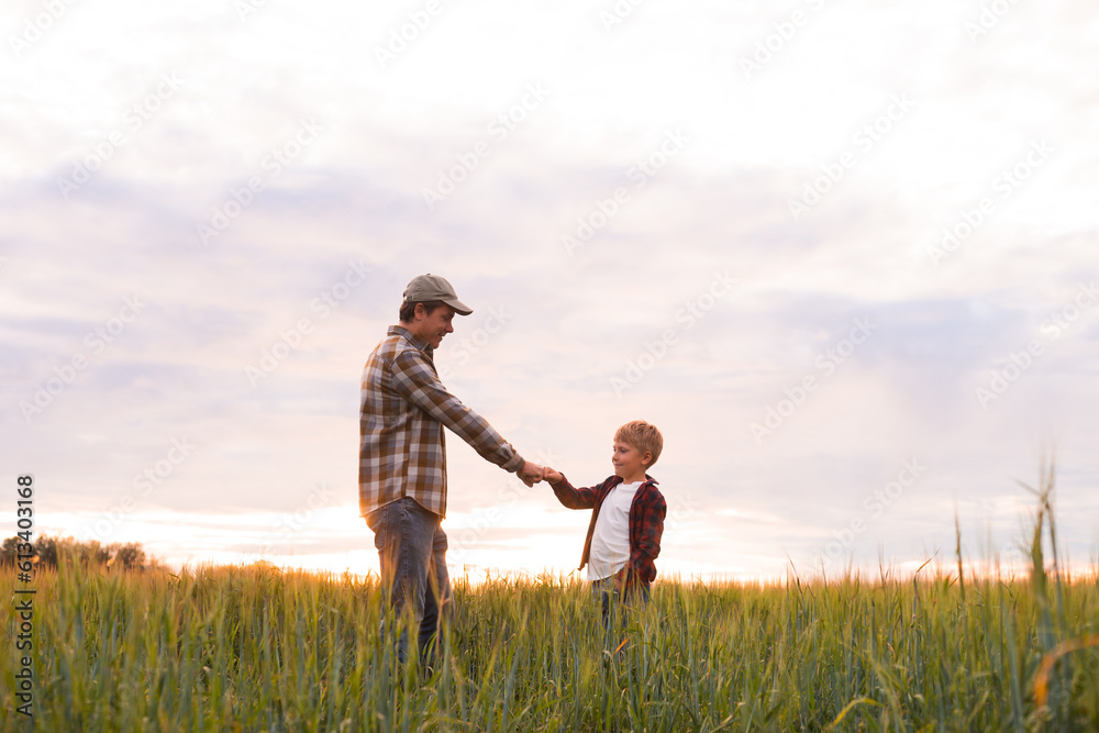 Farmer and his son in front of a sunset agricultural landscape. Man and a boy in a countryside field. Fatherhood, country life, farming and country lifestyle concept.