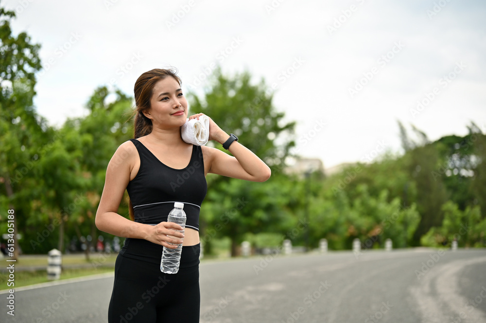 A fit Asian woman in sportswear wipes sweat from her face and neck with a towel A fit Asian woman in sportswear wipes sweat from her face and neck with a towel