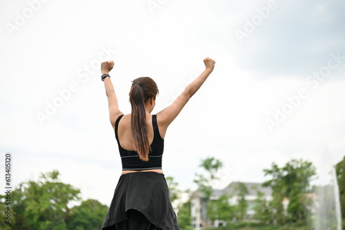 Back view, A sporty, carefree, and happy Asian woman raises her hands and rests after a long run