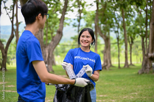 Two young Asian volunteers with garbage bag enjoy cleaning up an area in the public park
