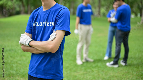 Cropped image of an Asian male volunteer in uniform stands in a public park with arms crossed. © bongkarn