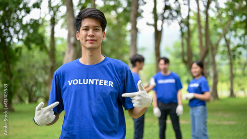 A happy Asian male volunteer stands in a public park, participating in volunteer work © bongkarn
