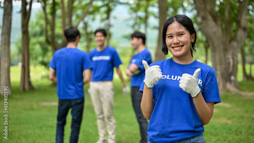 A beautiful Asian female volunteer stands in a public park and shows her thumbs up