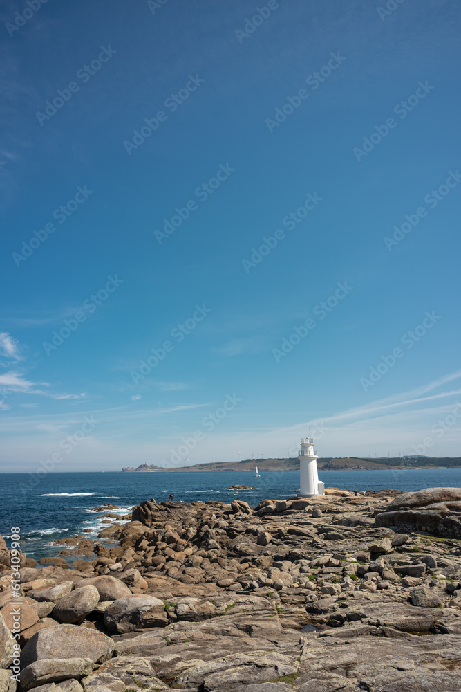 seascape of the rocky coastline on a blue sky day with a lighthouse on the sea shore
