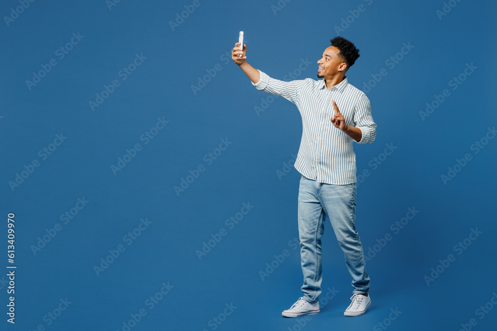 Full body young man of African American ethnicity wear casual clothes shirt do selfie shot on mobile cell phone post photo on social network isolated on plain dark royal navy blue background studio Full body young man of African American ethnicity wear casual clothes shirt do selfie shot on mobile cell phone post photo on social network isolated on plain dark royal navy blue background studio