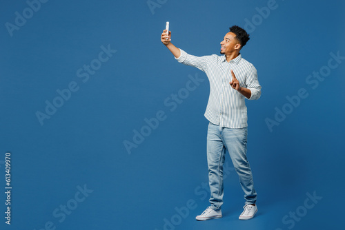 Full body young man of African American ethnicity wear casual clothes shirt do selfie shot on mobile cell phone post photo on social network isolated on plain dark royal navy blue background studio © ViDi Studio