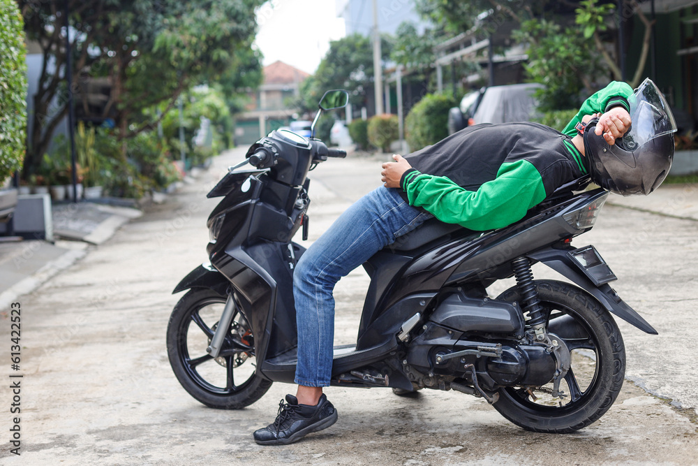 online transportation driver is laying on his parked scooter while waiting for an order, feeling tired and sleepy