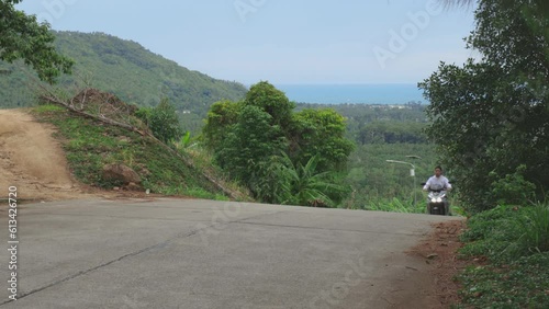 Guy on motorbike drives up a steep hill on Koh Samui, Thailand photo