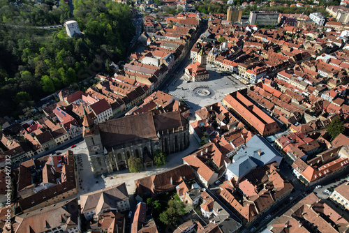 An aerial view of the Council Square in Brasov, Romania, against the backdrop of a sunny day. The image showcases the square's medieval buildings that stand as silent witnesses to the city's past.