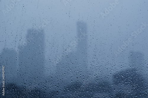 Rain drop on glass window in monsoon season with blurred city buildings background. photo