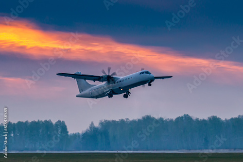 Take-off of a white passenger turboprop aircraft against the backdrop of a picturesque dawn sky