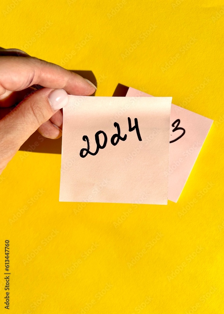 New Year 2024 written on note paper on a bright yellow background. Business concept. Plans for the new year. New Year 2024 written on note paper on a bright yellow background. Business concept. Plans for the new year.