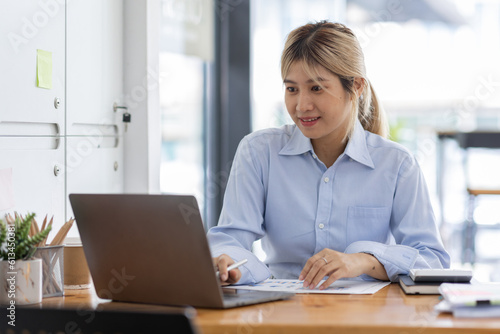 Asian Business woman using calculator and laptop for doing math finance on an office desk, tax, report, accounting, statistics, and analytical research concept 