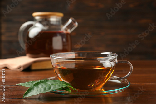 Cup of aromatic tea, green leaves and teapot on wooden table, closeup