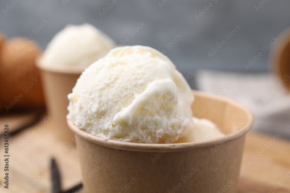 Paper cups with delicious ice cream and vanilla pods on wooden board, closeup