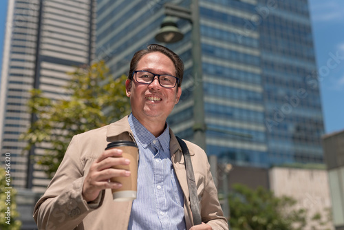 A middle aged office worker in his 40s holding a cup of coffee. Walking through the city, with office towers in the background.