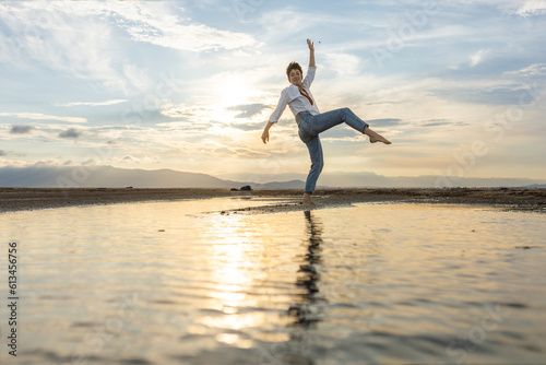 woman on the beach dancing at sunset in backlight with the sun behind in shadow, woman on vacation walking on the sand with golden water reflections from the sun at sunset