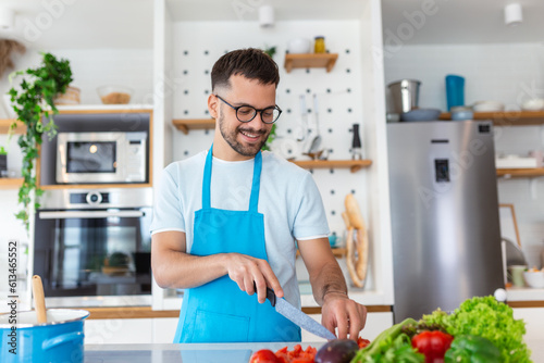 Handsome young man man stand at modern kitchen chop vegetables prepare fresh vegetable salad for dinner or lunch, young male cooking at home make breakfast follow healthy diet, vegetarian concept