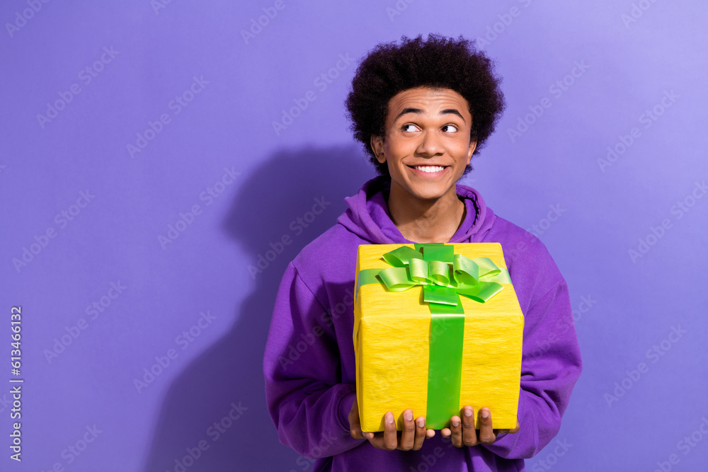 Portrait of positive minded man toothy smile arms hold giftbox look interested empty space isolated on purple color background Portrait of positive minded man toothy smile arms hold giftbox look interested empty space isolated on purple color background