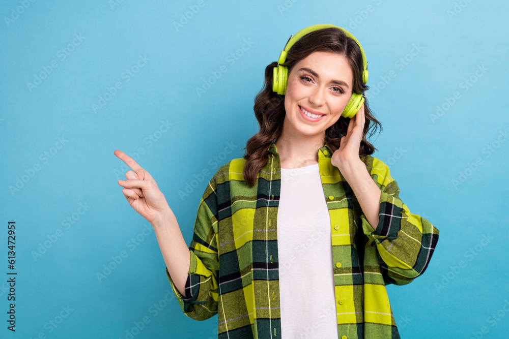 Portrait of satisfied toothy beaming girl wear plaid jacket touching headphones indicating empty space isolated on blue color background Portrait of satisfied toothy beaming girl wear plaid jacket touching headphones indicating empty space isolated on blue color background