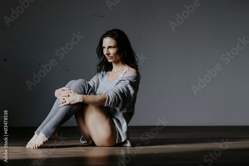 Sportliche, dunkelhaarige Frau sitzt im gemütlichen Outfit am Boden