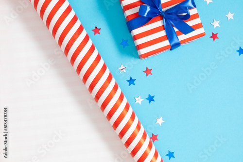 Fototapeta Naklejka Na Ścianę i Meble -  4th of July, USA Presidents Day, Independence Day. Flat lay top view of patriotic wrapping paper and gift box twinkling confetti on blue background with space, promotion or greeting message, banner