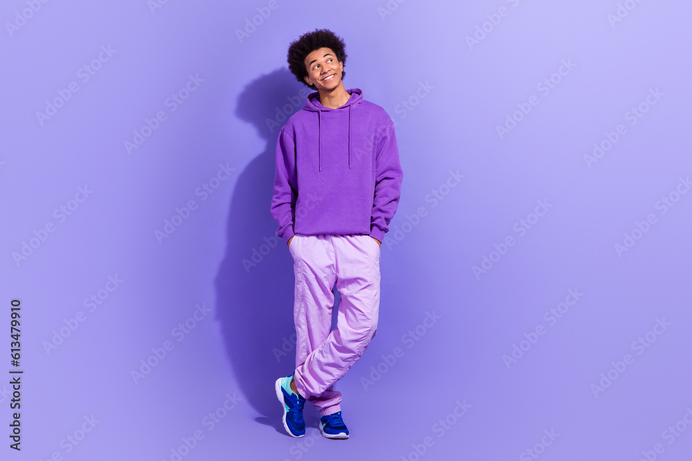 Full body photo of creative minded cheerful young man put arms pockets look empty space isolated on violet color background Full body photo of creative minded cheerful young man put arms pockets look empty space isolated on violet color background