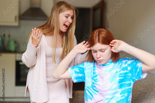 Family conflict and relations concept. Mother and daughter having quarrel and aguring at home. Sad woman and teenage girl close ears with hands. 