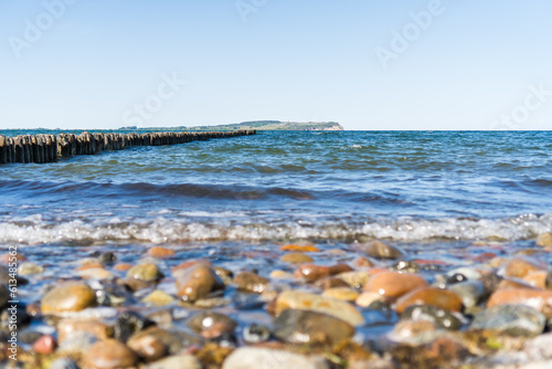 View from stony beach on German island Rugia towards Hiddensee with groyne and waves in the foreground