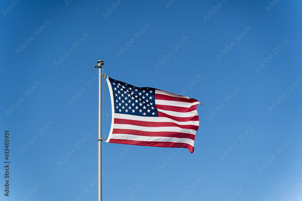 The flag of the United States of America flutters in the wind against a clear blue sky. Waving USA flag