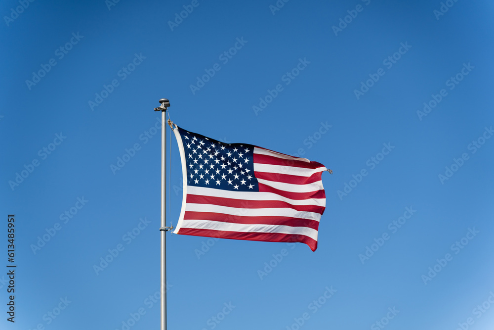 The flag of the United States of America flutters in the wind against a clear blue sky. Waving USA flag The flag of the United States of America flutters in the wind against a clear blue sky. Waving USA flag