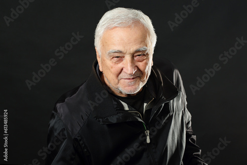Emotional portrait of a handsome senior man, smiling at the camera, looking joyful and positive. Studio shot of a happy, slightly bearded European elder person with white hair against dark background