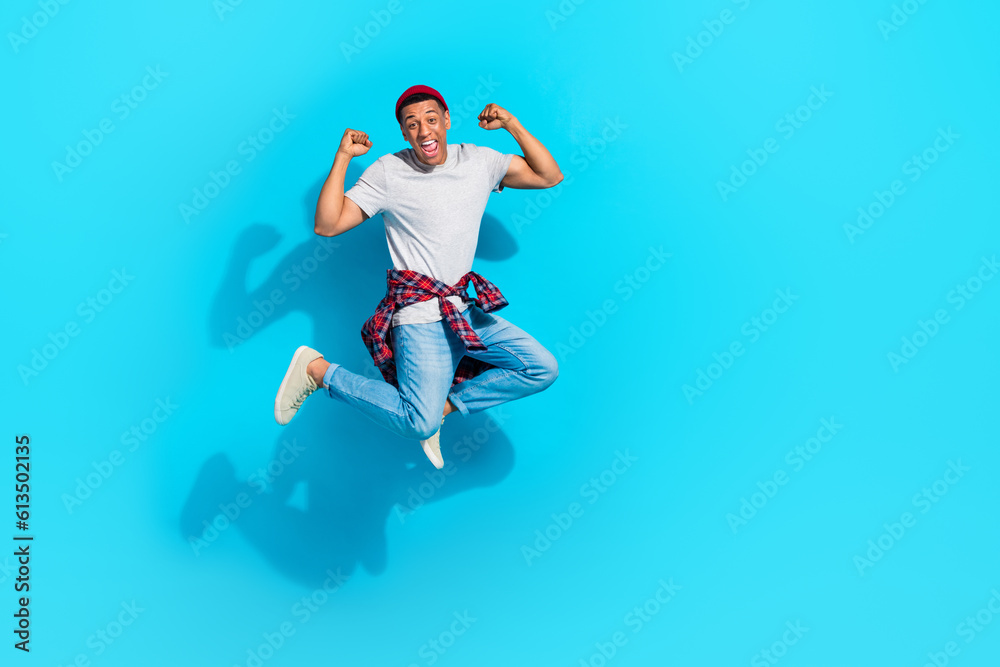 Full size photo of delighted excited man jumping raise fists achieve triumph empty space isolated on blue color background
