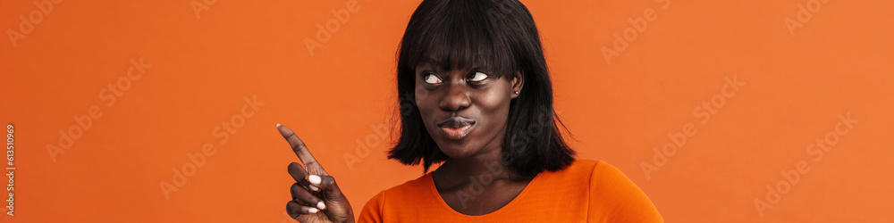 Image of cute african lady pointing aside over orange background Image of cute african lady pointing aside over orange background