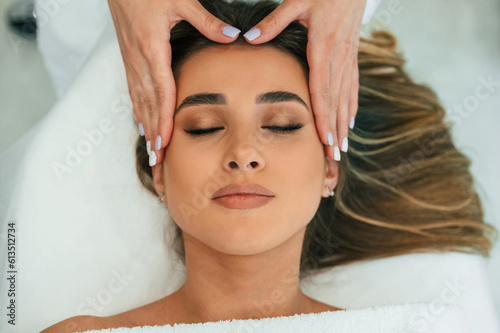 With eyes closed, doing massage. Woman face getting facial care by beautician hands at spa salon