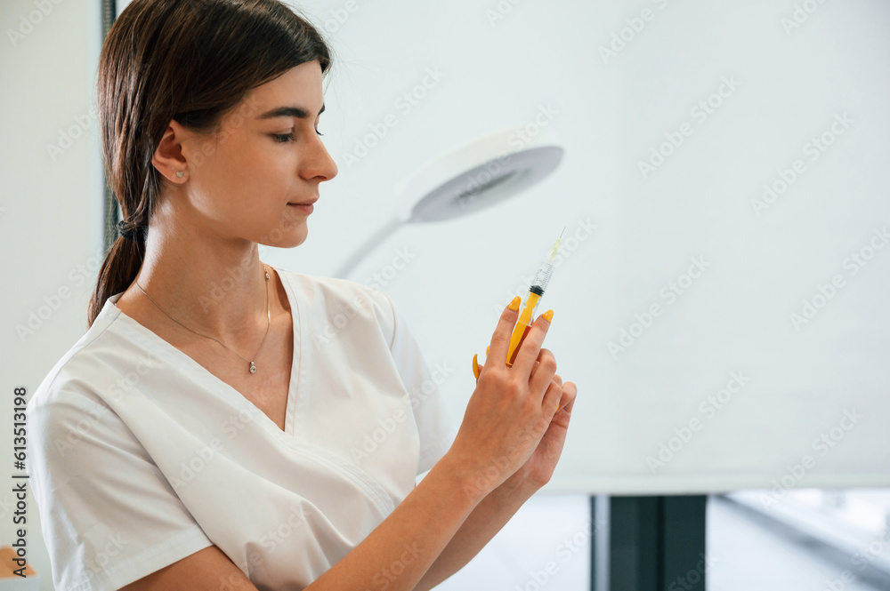 Young beautician is standing indoors and holding syringe Young beautician is standing indoors and holding syringe