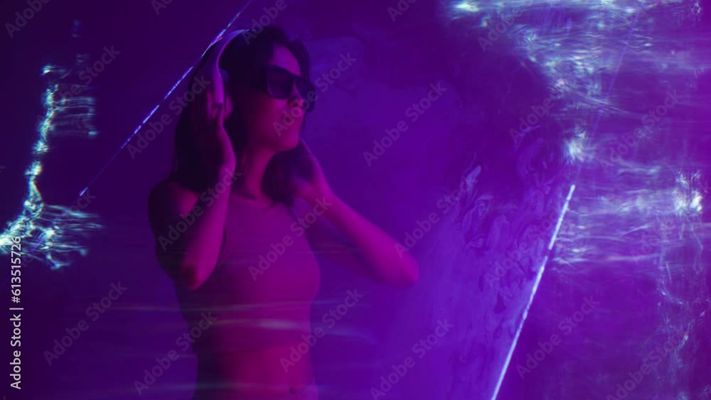 Beautiful woman with purple hair in futuristic costume over dark background. Violet neon light. Portrait of young girl in modern headphones listening music. Beautiful woman with purple hair in futuristic costume over dark background. Violet neon light. Portrait of young girl in modern headphones listening music.