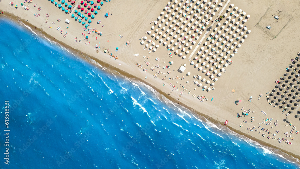The coastline of the sea with a sandy clean beach and colored umbrellas is located diagonally across the frame. Shooting from a drone
