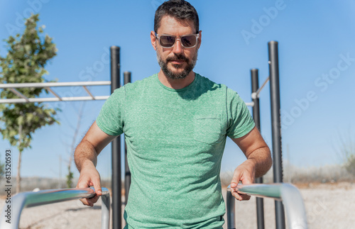 Fotografia man with beard and sunglasses training his arms on parallel bars in a park gymn
