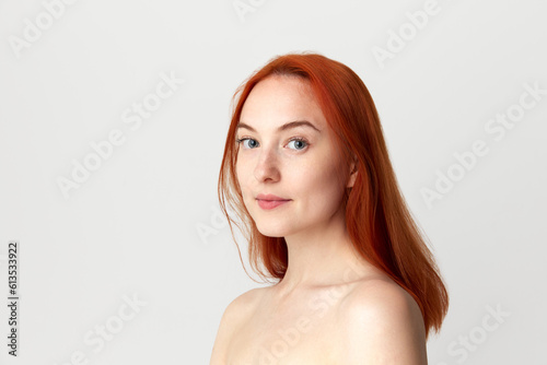 Young Caucasian beautiful girl with perfect skin and healthy red hair posing over light studio background.