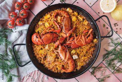 spanish seafood paella with lobster and squid, traditional dish with rice, top view of a hot pot, surrounded by fresh ingredients on a pink background table