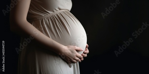 Pregnant woman in dress holds hands on belly on a dark background. Pregnant woman touching belly. Pregnancy, maternity photo, preparation and expectation concept