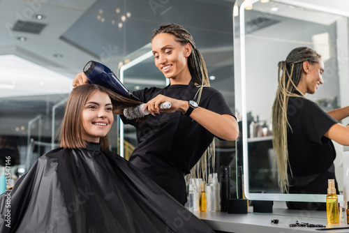 beauty salon, professional beauty worker with round brush and hair dryer styling hair of happy customer, brunette woman with short hair, salon blow dry, client satisfaction, hair volume