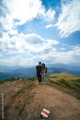 Couple woman and man wearing wide sun hat and backpack, tourists on hiking trail to Koruldi Lakes, Svaneti region, Mestia Georgia. The concept of travel and active recreation. Vertical photo