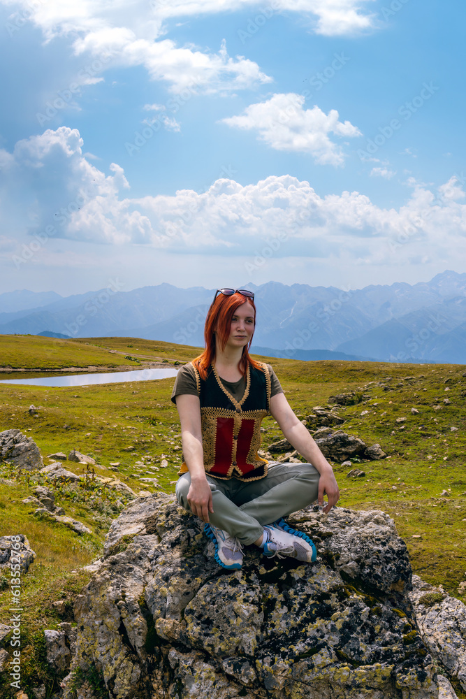 Naklejka premium Portrait of a young woman sitting in the lotus position on a rock boulder. Practices yoga. Vertical photo, Georgia. Summer day in the mountains of the Caucasus. Spiritual mood and relaxation